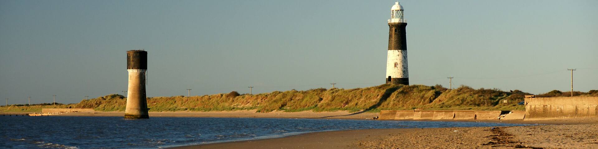 A coastal scene with two lighthouses, a sandy beach, and a grassy hill in the background.