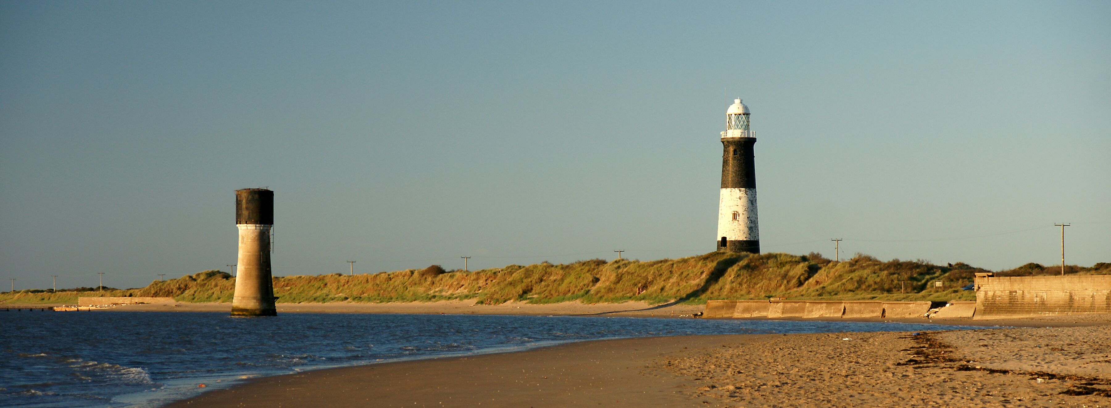 A coastal scene with two lighthouses, a sandy beach, and a grassy hill in the background.