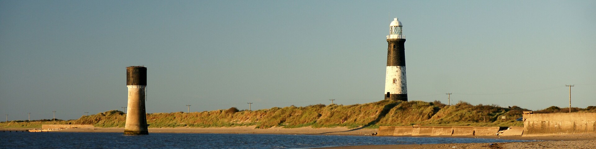 A coastal scene with two lighthouses, a sandy beach, and a grassy hill in the background.