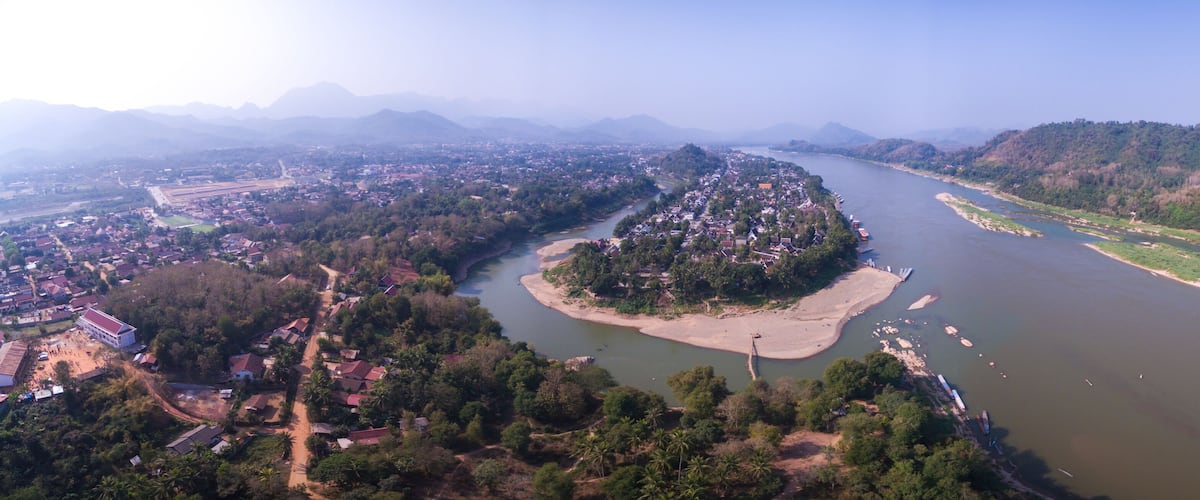 An aerial view of a river with a small island, surrounded by hills and a town.