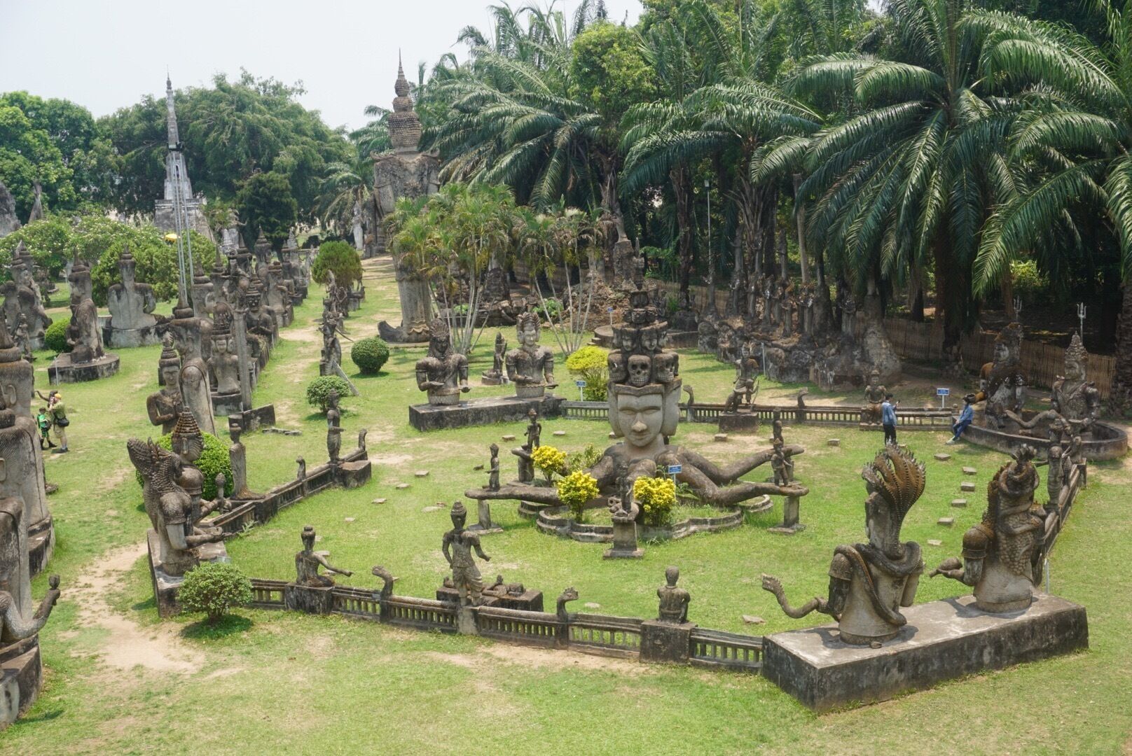A temple complex with numerous statues and a central Buddha statue surrounded by palm trees.