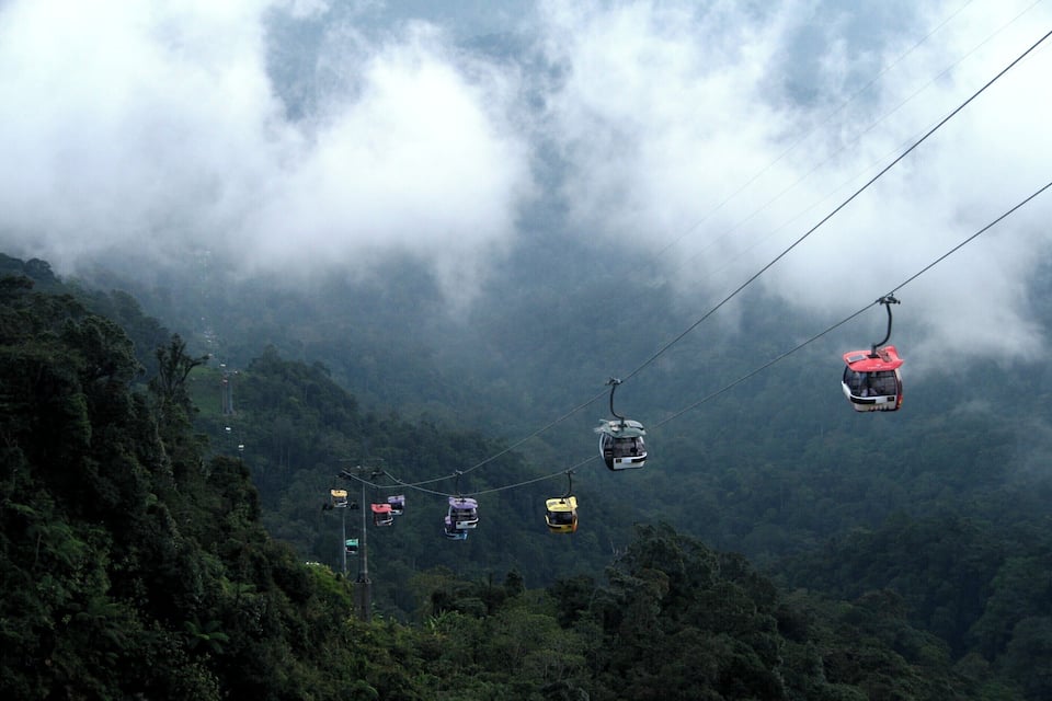 A cable car system in a mountainous area with lush greenery and clouds in the background.