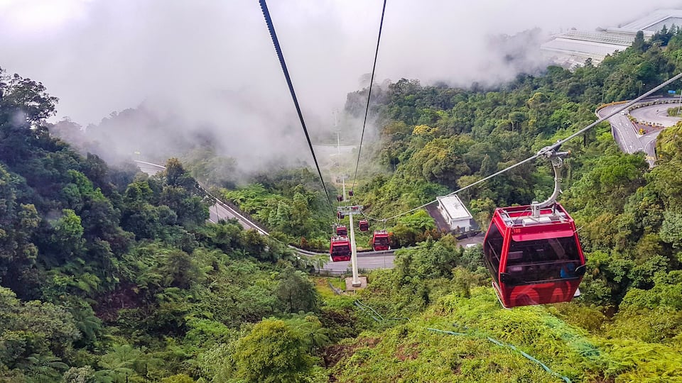 A cable car system in a lush, mountainous area with dense greenery and mist.