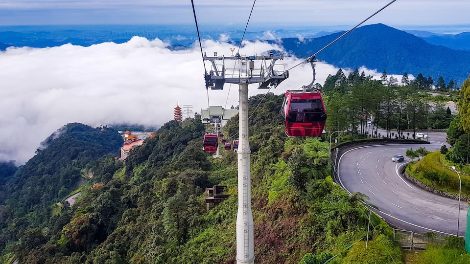 A cable car system, winding roads, and lush green hills with a distant view of a city.