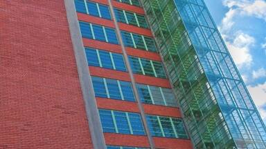 A tall building with a red brick facade and a glass structure.