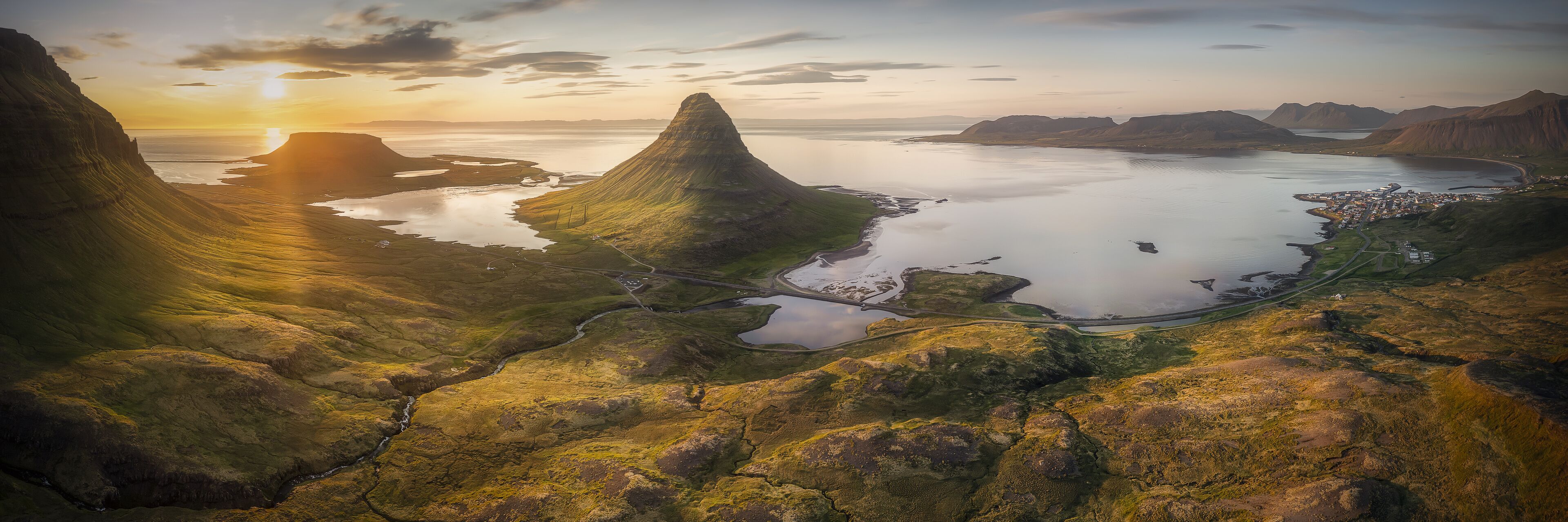 A coastal landscape with a prominent mountain peak, a winding road, and a small settlement by the water.