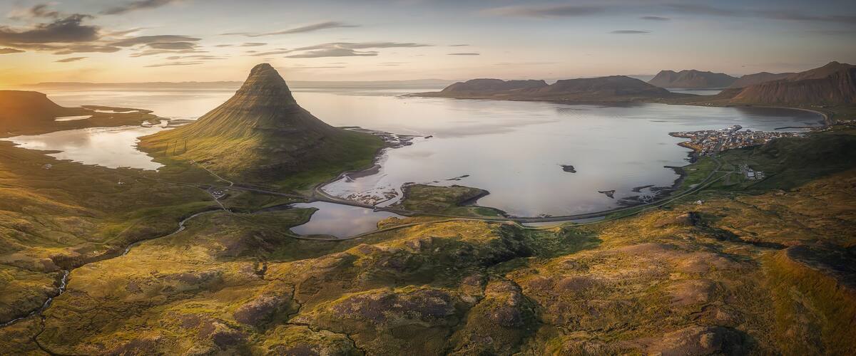 A coastal landscape with a prominent mountain peak, a winding road, and a small settlement by the water.
