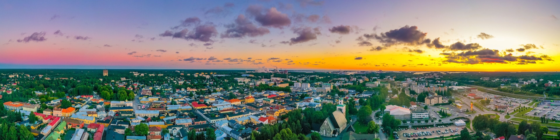 Vista panorâmica de uma cidade ao pôr do sol, com uma mistura de edifícios coloridos e áreas verdes.