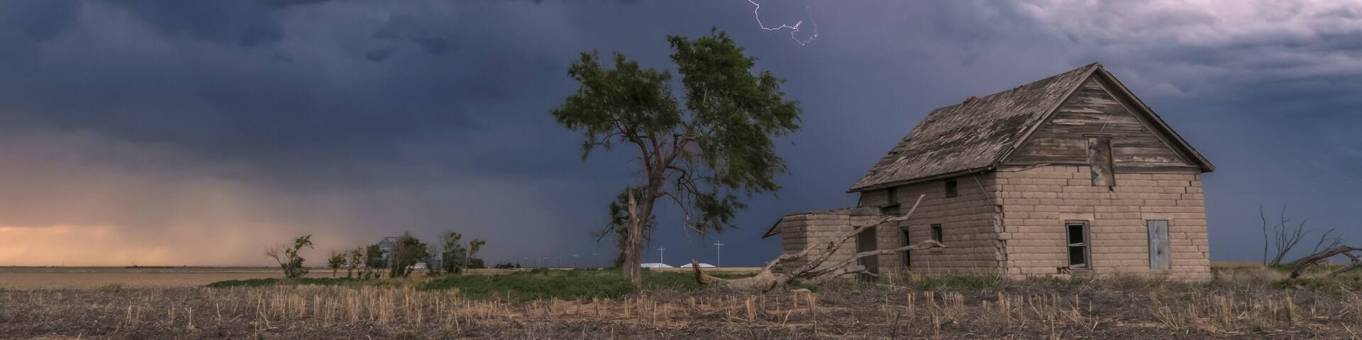 A forked lightning bolt descends from a weak thunderstorm near an abandoned building; Guymon, Oklahoma, United States of America