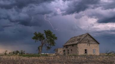 A forked lightning bolt descends from a weak thunderstorm near an abandoned building; Guymon, Oklahoma, United States of America