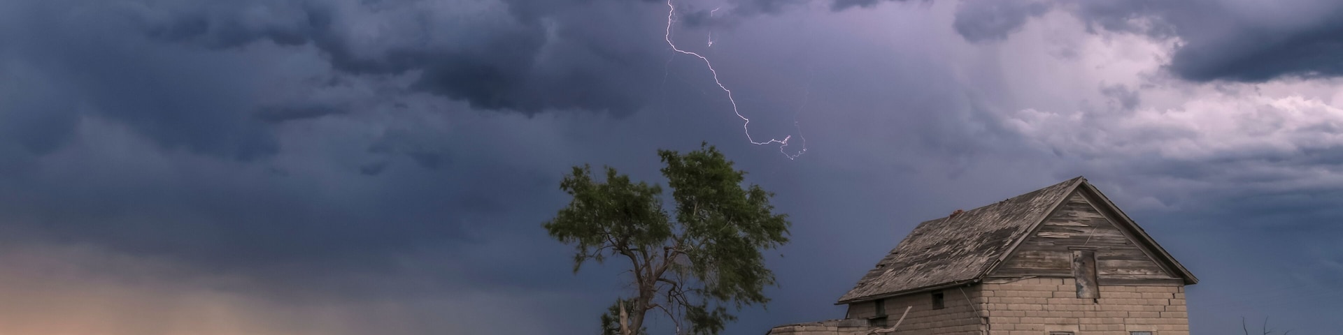 A forked lightning bolt descends from a weak thunderstorm near an abandoned building; Guymon, Oklahoma, United States of America