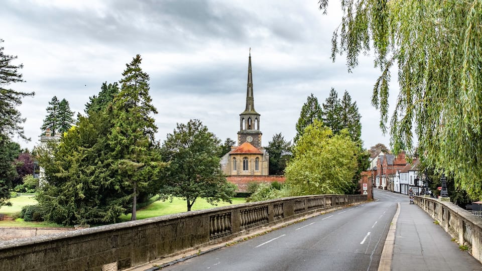 A church with a tall spire, surrounded by trees and a stone bridge.