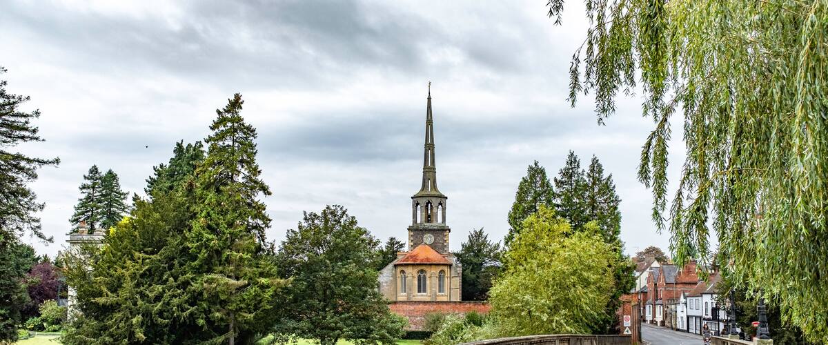 A church with a tall spire, surrounded by trees and a stone bridge.