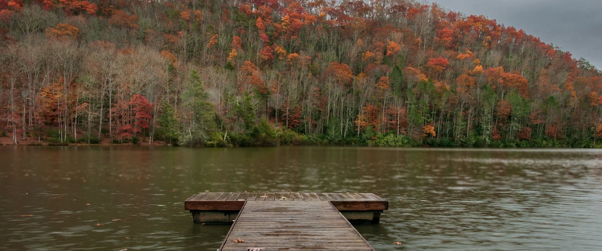 A wooden pier extending into a calm lake, surrounded by a forest with autumn-colored trees.
