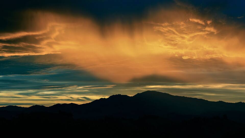 A mountain range silhouetted against a sunset sky with dramatic cloud formations.