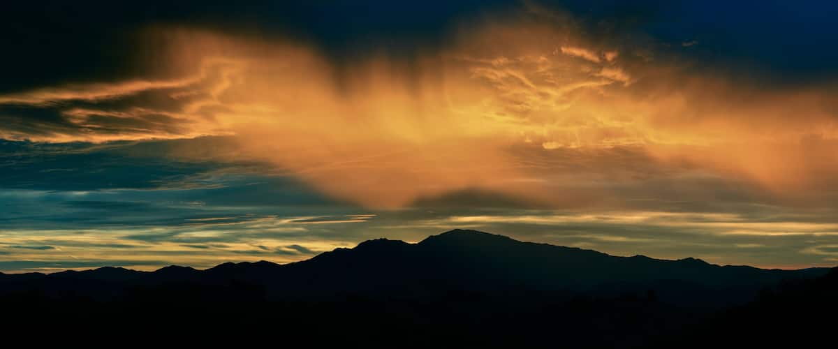 A mountain range silhouetted against a sunset sky with dramatic cloud formations.