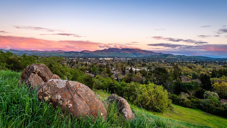 A mountainous landscape with a town in the valley, large rocks, and lush greenery.
