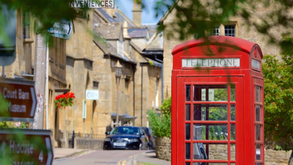A red telephone booth in a quaint village with stone buildings and signs for a museum and a court barn.