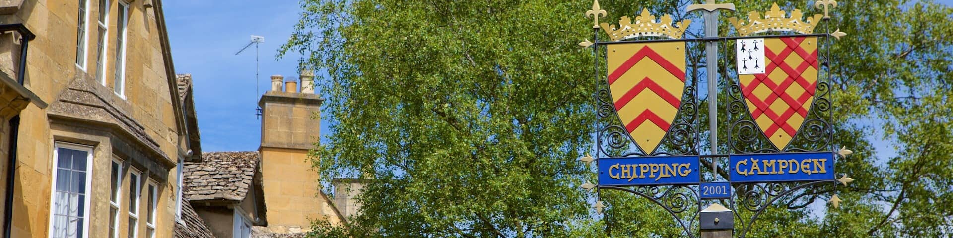 A street sign with two shields, one labeled 'Chipping' and the other 'Camden', mounted on a pole with a cross at the top.