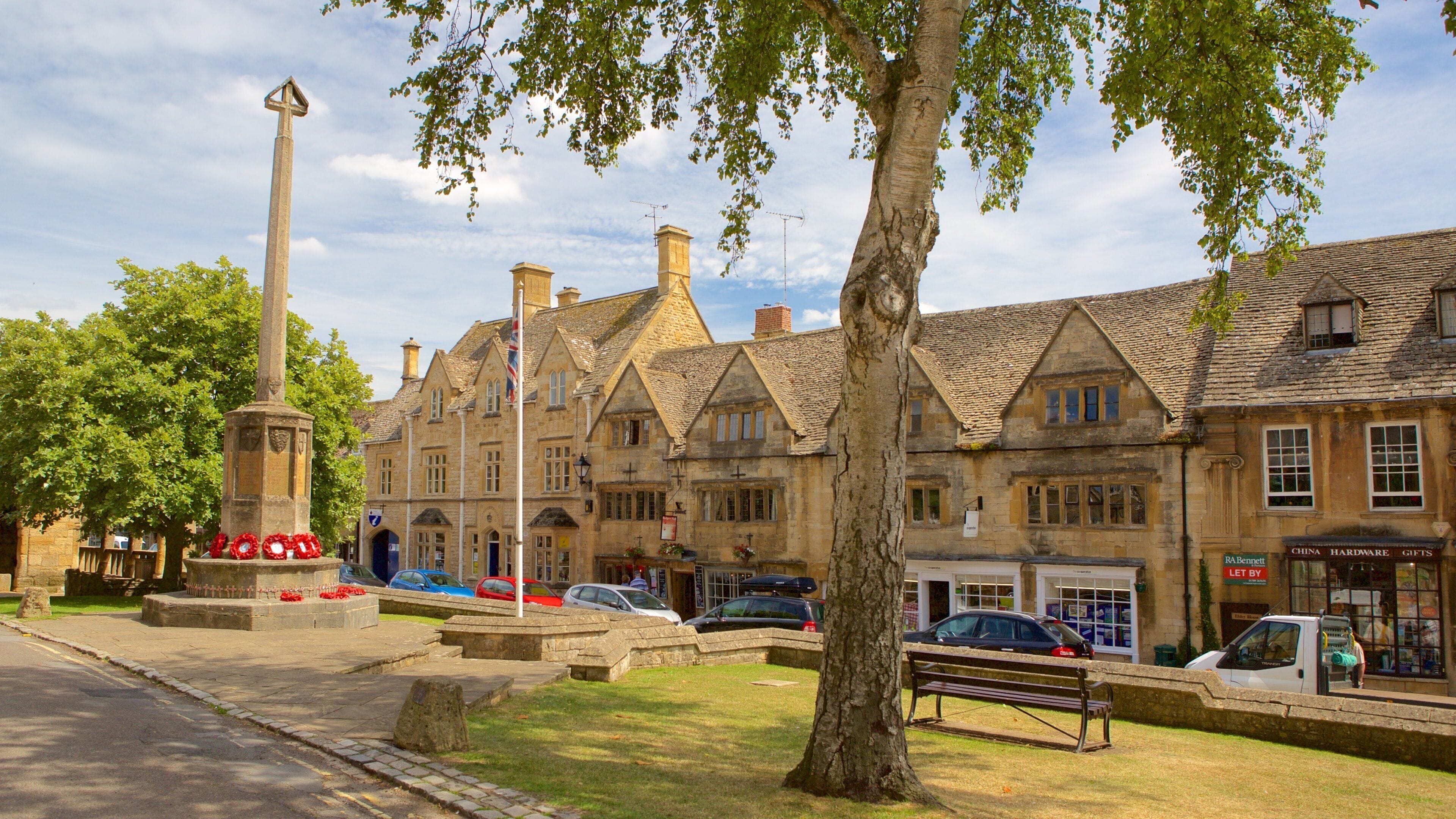 A historic town square with a tall monument, stone buildings, and a tree.