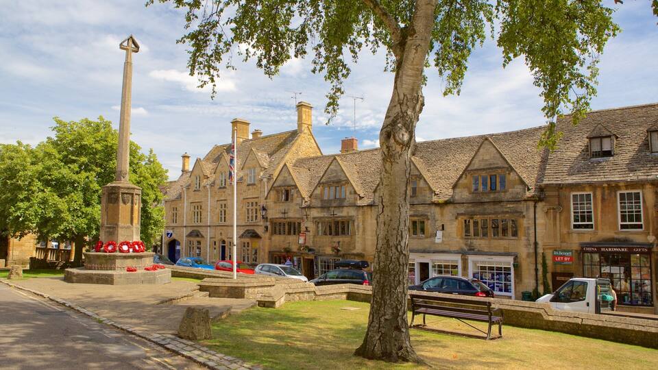 A historic town square with a tall monument, stone buildings, and a tree.