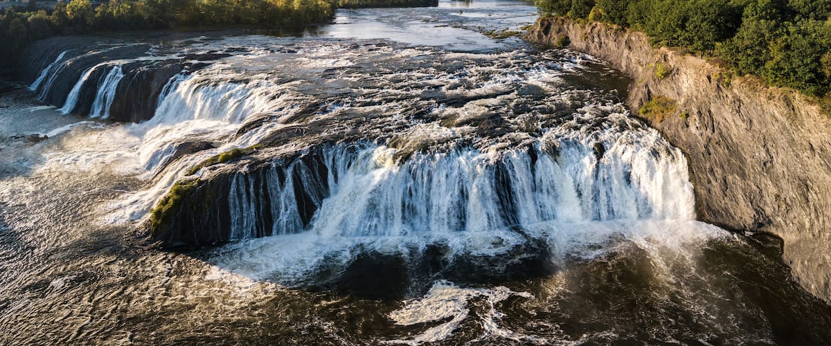 A multi-tiered waterfall cascading down a rocky cliff surrounded by dense forest.