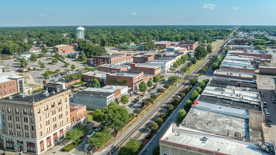A cityscape with a railroad track running through the center, surrounded by buildings and greenery.