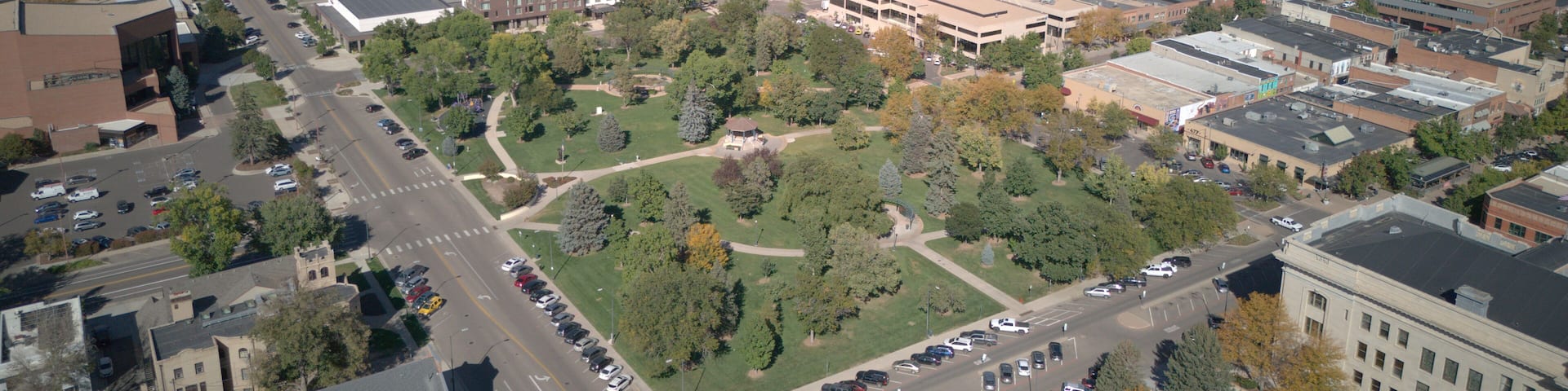 Aerial view of Lincoln Park's lush greenery and surrounding buildings under a clear blue sky, a vibrant contrast to the urban landscape, Greeley, Colorado, United States.