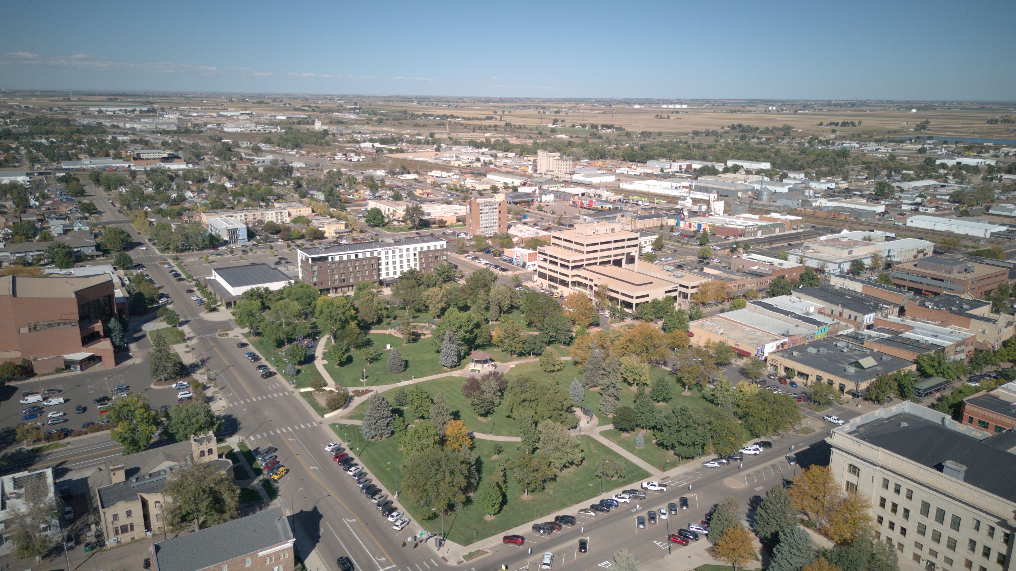 An aerial view of a city with a central park, various buildings, and a distant view of fields.
