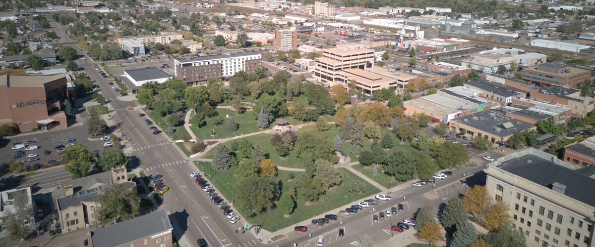 An aerial view of a city with a central park, various buildings, and a distant view of fields.