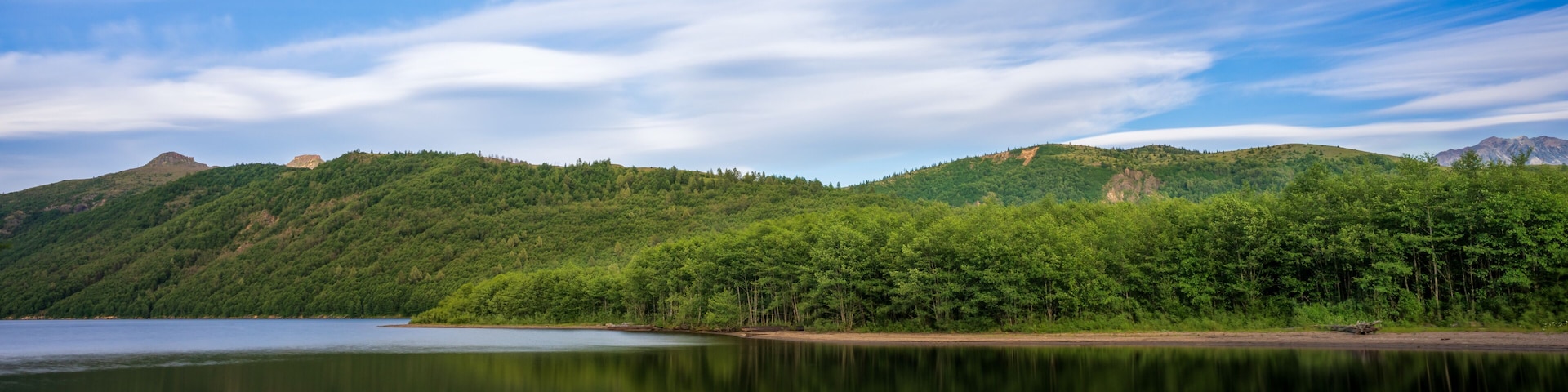 Un lago tranquilo que refleja el cielo y la vegetación circundante, con colinas al fondo.