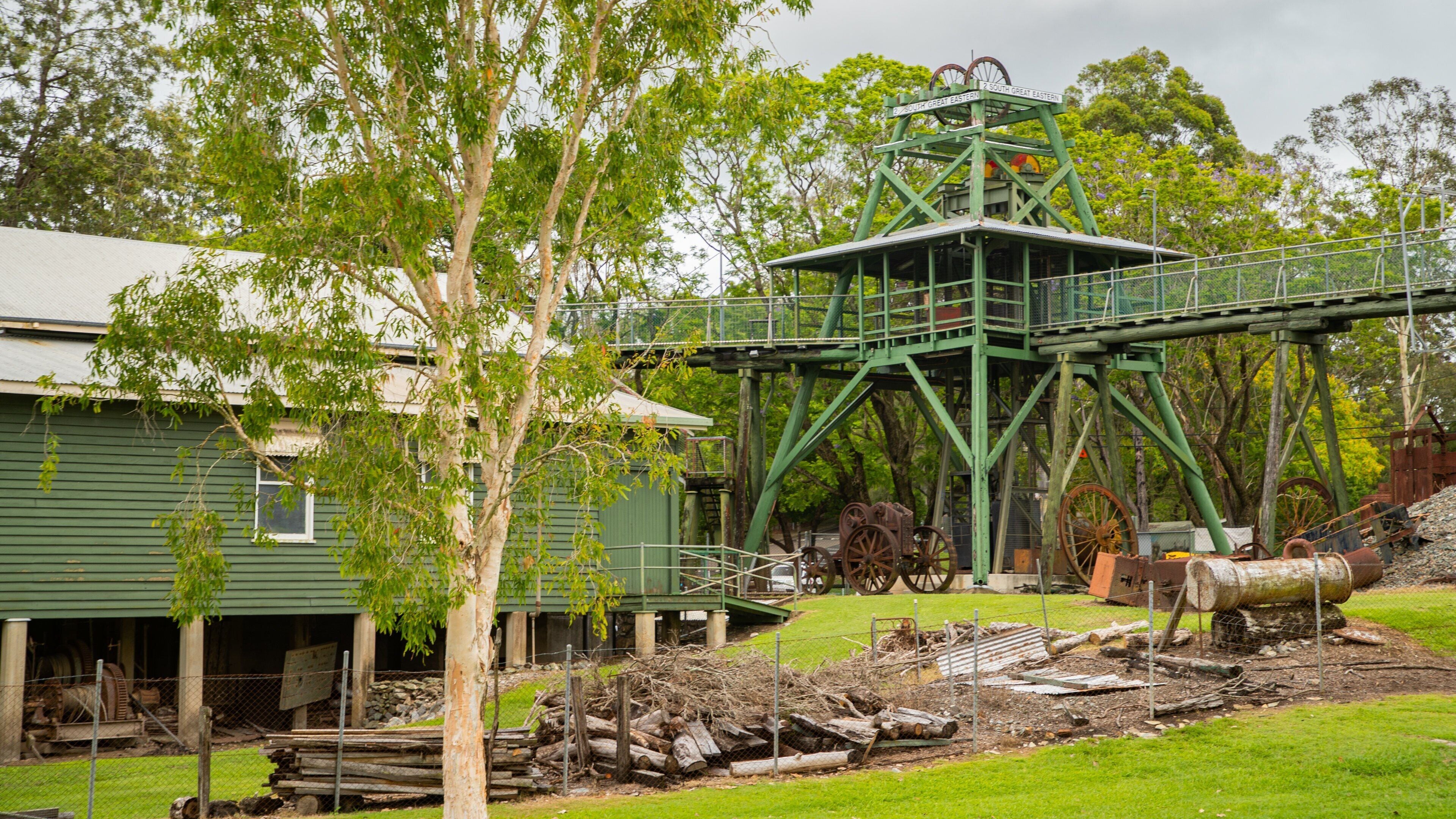 A green metal structure with wheels, a green building, and trees.
