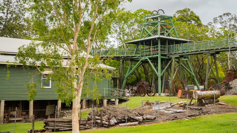 A green metal structure with wheels, a green building, and trees.