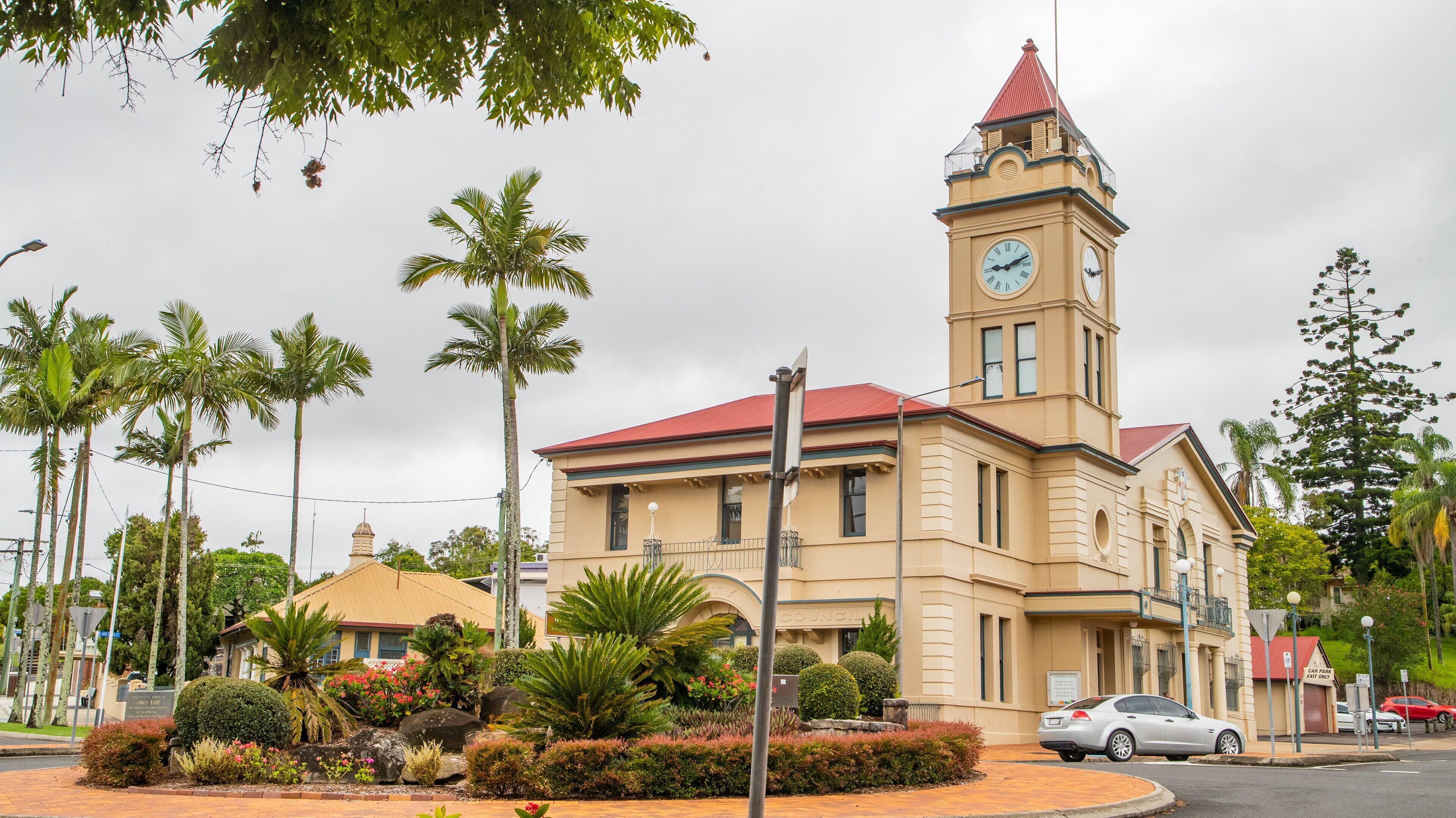 A historic building with a clock tower, surrounded by palm trees and a landscaped garden.