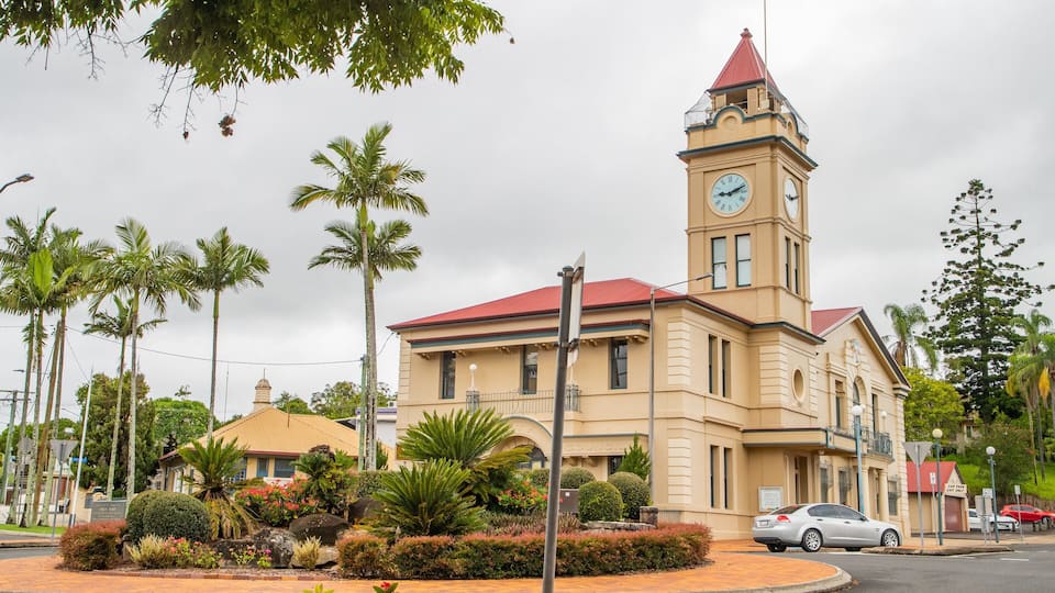 A historic building with a clock tower, surrounded by palm trees and a landscaped garden.