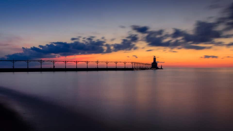 A pier extending into calm waters at sunset with a clear sky.