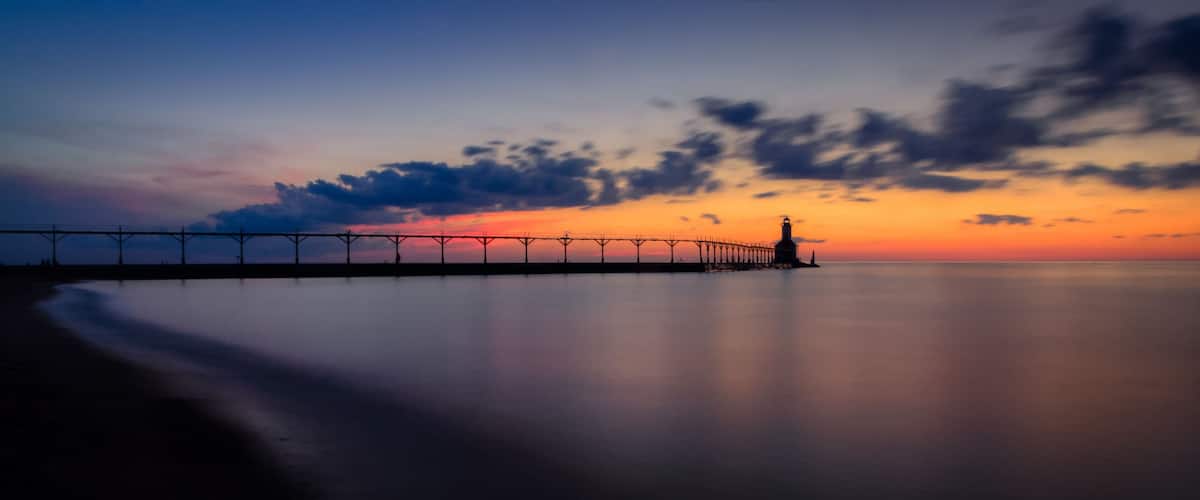 A pier extending into calm waters at sunset with a clear sky.