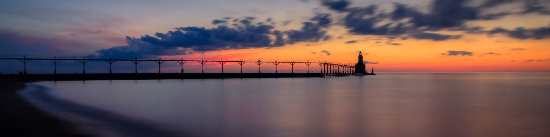 A pier extending into calm waters at sunset with a clear sky.