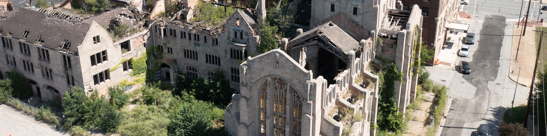 Aerial view of the historic ruins of the City Methodist Church with overgrown vegetation and crumbling stone walls surrounded by urban buildings in Gary, Indiana, United States.
