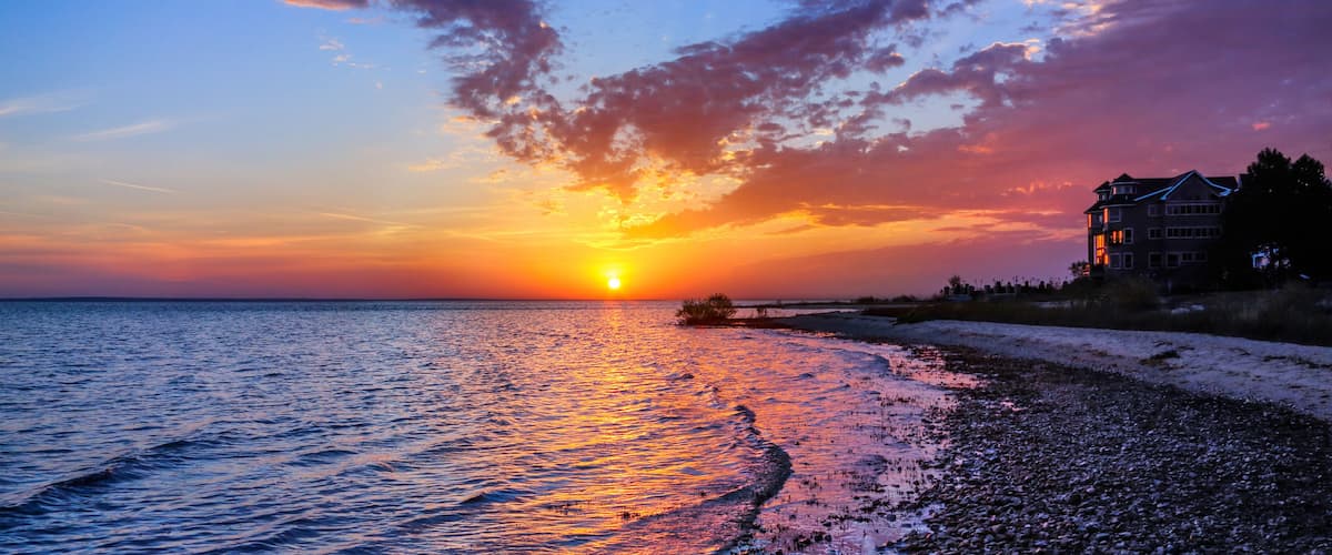 A sunset over a beach with a house on the right.