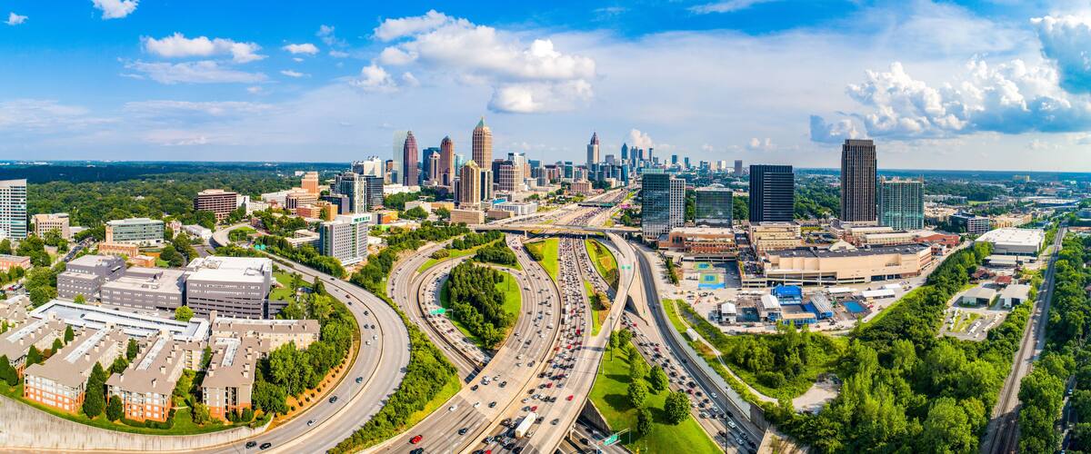 A city skyline with a mix of modern and older buildings, a highway with multiple lanes, and surrounding greenery.