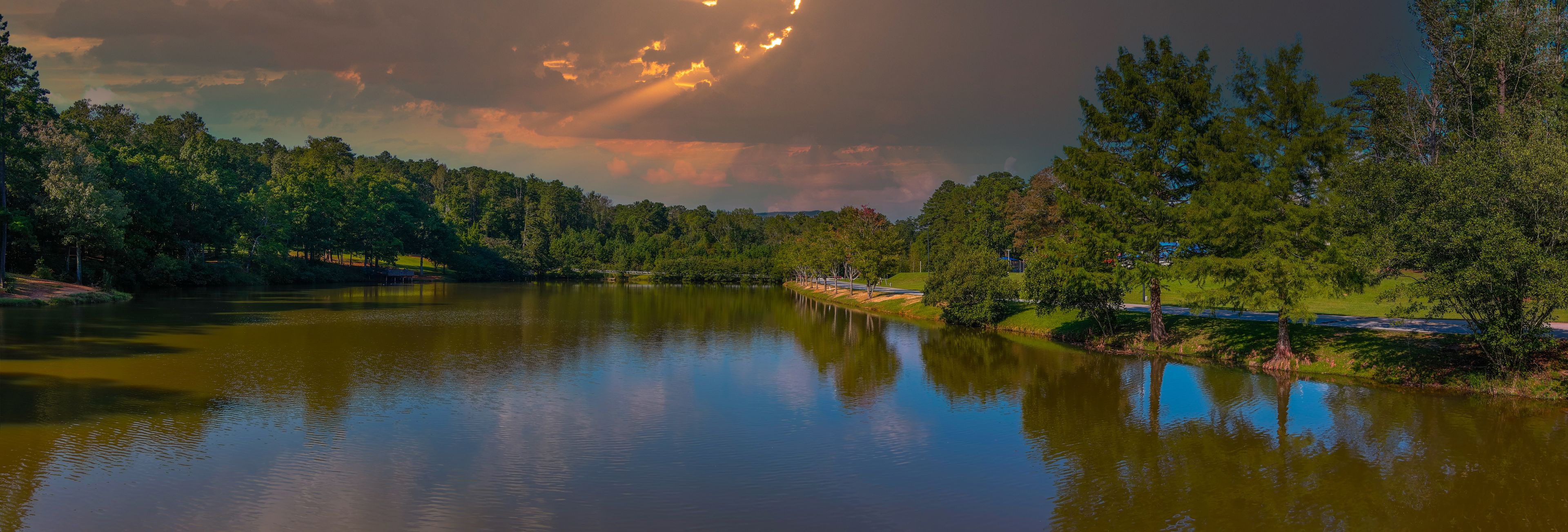 a stunning aerial panoramic shot of the still green lake surrounded by lush green and autumn colored trees with powerful clouds at sunset at Duncan Park in Fairburn Georgia USA