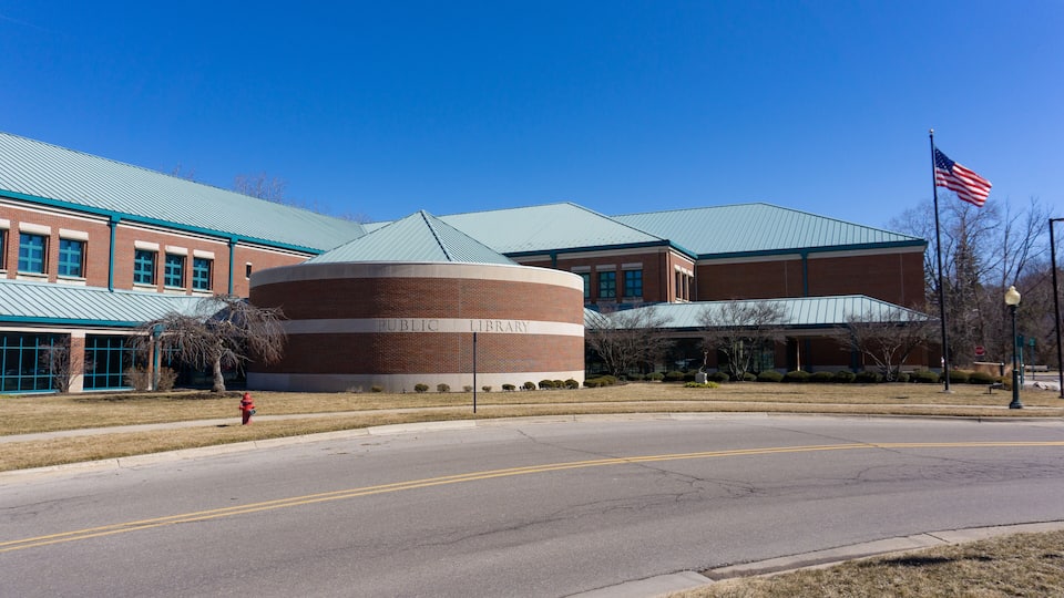 A public library with a brick facade, a circular building, and an American flag.