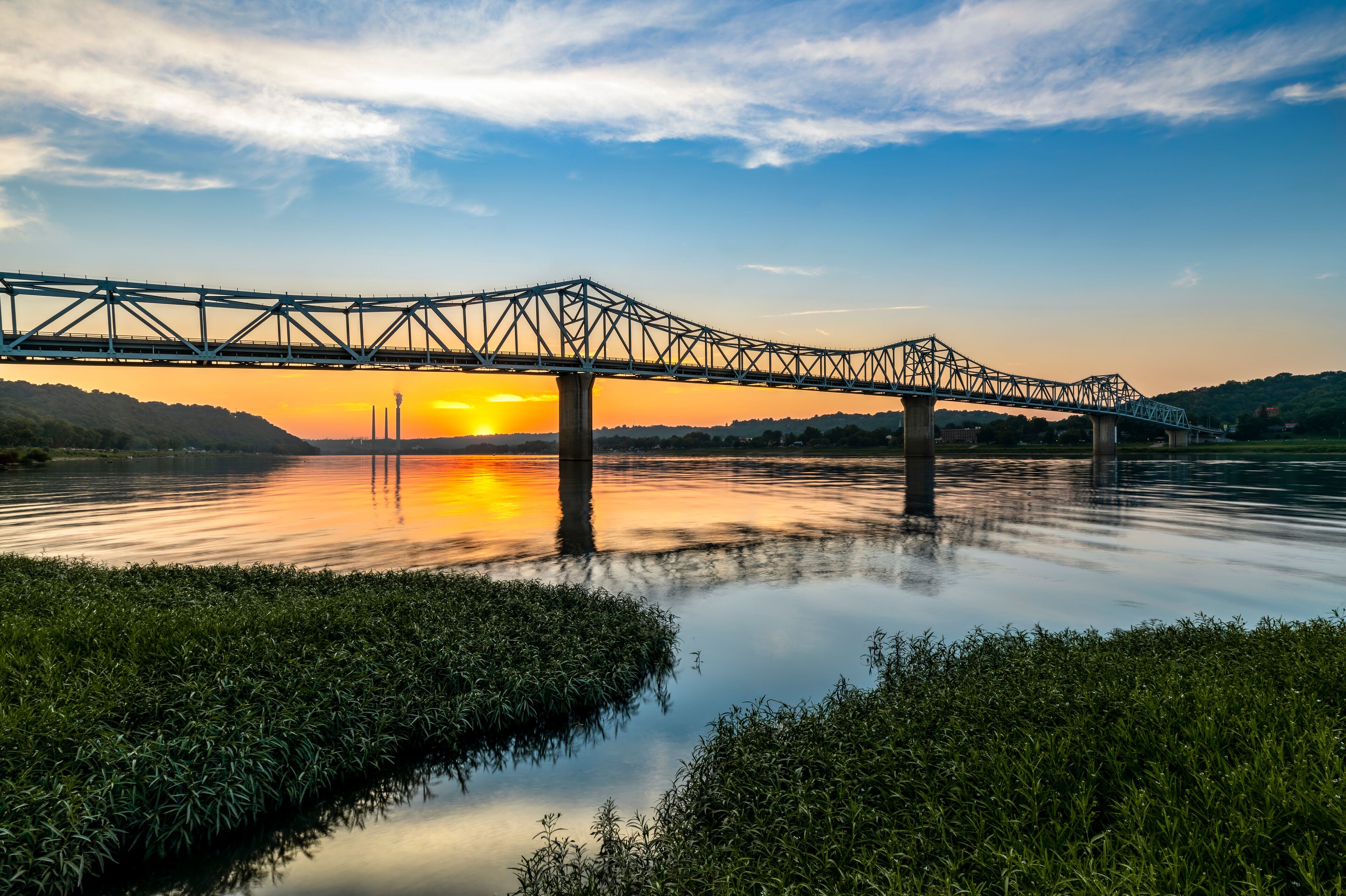 A steel bridge over a calm river at sunset.