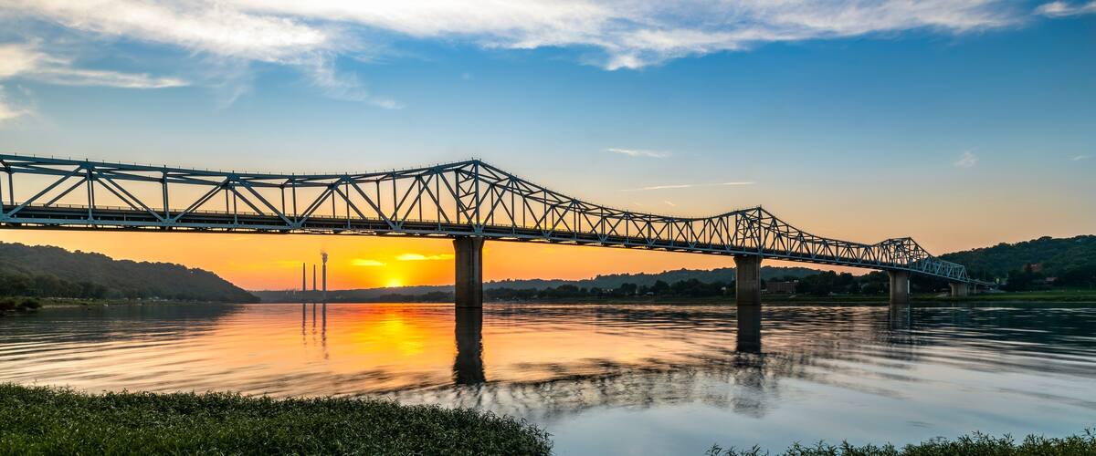 A steel bridge over a calm river at sunset.