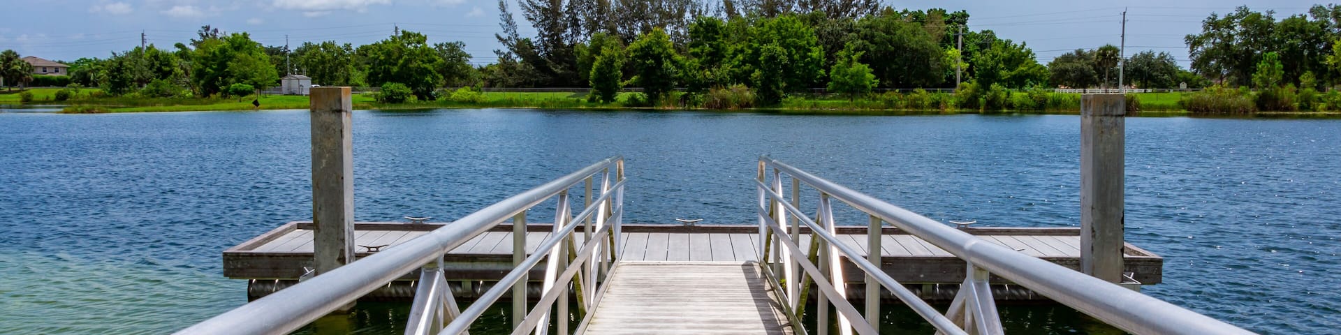 Ramp to boat dock on blue green lake with trees, vegetation and blue sky - Vista View Park, Davie, Florida, USA