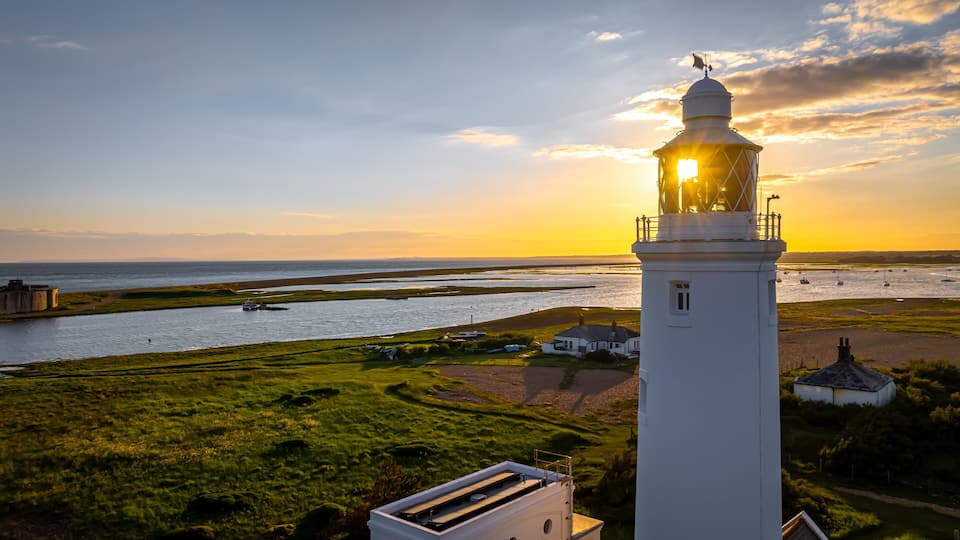 A lighthouse, a river, and a coastal landscape during sunset.