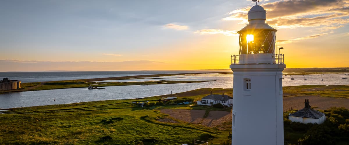 A lighthouse, a river, and a coastal landscape during sunset.