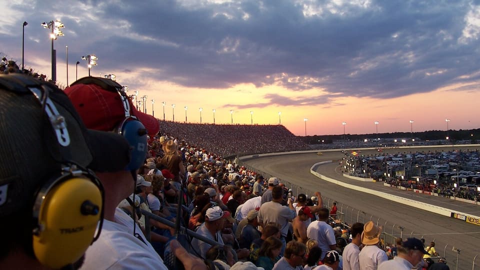 A crowded racetrack at sunset with a large audience.