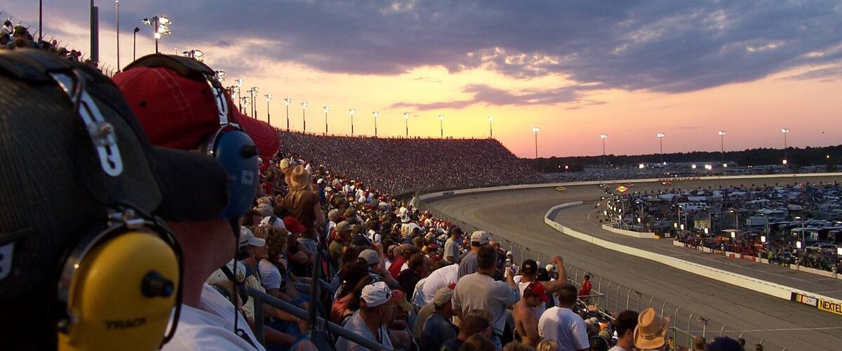 A crowded racetrack at sunset with a large audience.